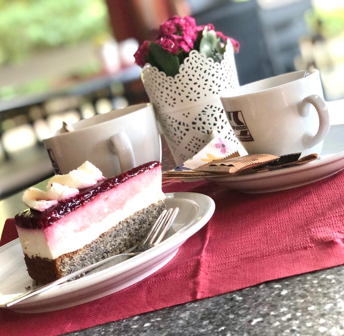 Saftiges Tortenstück auf einem Cafétisch neben einer dampfenden Tasse Kaffee